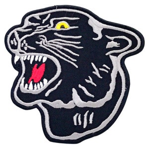 Op de afbeelding: Zwarte en witte geborduurde patch van een brullende panterkop met een geel oog. De bek van de panter is open en zijn tanden zijn zichtbaar. De patch is perfect om een ​​tikje wildheid toe te voegen aan je kleding of accessoires.