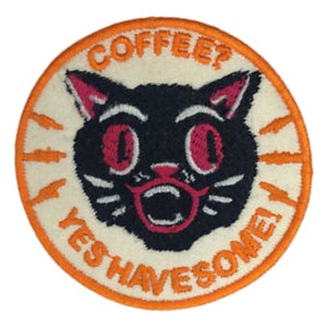 May include: A white and orange embroidered patch featuring a black cat with red eyes and a pink mouth. The text on the patch reads "Coffee? Yes Have Some!"