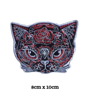 May include: Black and red embroidered iron-on patch of a cat's face with a diamond in the center. The cat's eyes are detailed with white and black stitching. The patch is 8 cm by 10 cm.