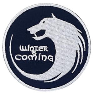 Può includere: Un cerotto circolare nero con un lupo mannaro bianco e il testo "Winter is Coming" in bianco.