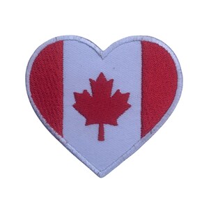 May include: A red heart-shaped patch with the Canadian flag. The flag features a white field with a red maple leaf in the center and two red vertical stripes on the sides.