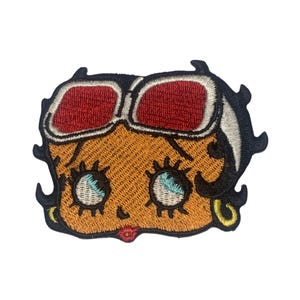May include: Embroidered patch featuring a cartoon character with red sunglasses, orange skin, and blue eyes. The character has a white headband and black hair.