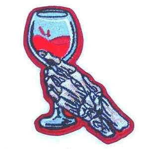 May include: A skeleton hand holding a glass of red wine. The glass is filled with red liquid and has a clear stem. The hand is white and has visible bones. The background is red.