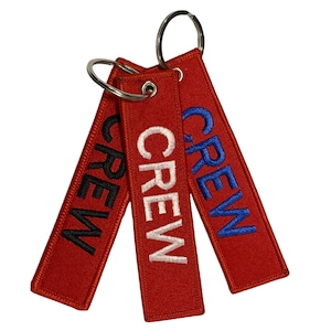 Pode incluir: Três chaveiros vermelhos com a palavra "CREW" bordada em preto, branco e azul.