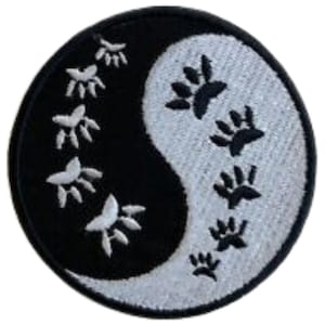 May include: Black and white yin yang symbol with paw prints around the edges. The yin yang symbol is embroidered on a black and white fabric.