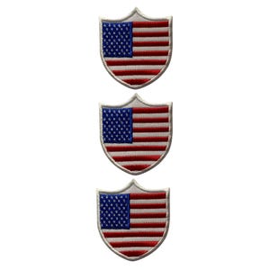 May include: Three embroidered shield-shaped patches, each displaying the American flag. The patches have a white border, a blue field with white stars, and red and white stripes. These patches are suitable for clothing or accessories.