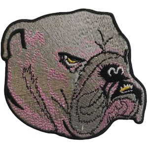 Puede incluir: Parche bordado de la cabeza de un bulldog gris con detalles rosas alrededor del hocico y las orejas. El bulldog tiene una expresión feroz con la nariz negra y los ojos amarillos.