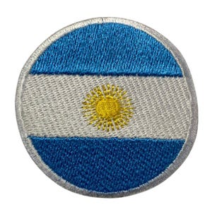 Può includere: Una toppa rotonda ricamata con la bandiera dell'Argentina. La toppa è blu, bianca e gialla con un sole al centro.