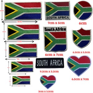 Può includere: Una collezione di toppe ricamate con la bandiera sudafricana in varie forme e dimensioni. Sono esposte toppe rettangolari, circolari, a scudo e a forma di cuore, con dimensioni comprese tra 3 cm e 18 cm di lunghezza. Le toppe presentano i colori della bandiera: rosso, verde, blu, giallo e nero.