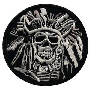 May include: A black and white embroidered patch featuring a skull with a headdress. The skull is surrounded by a white feathered headdress. The patch is circular and has a black border.