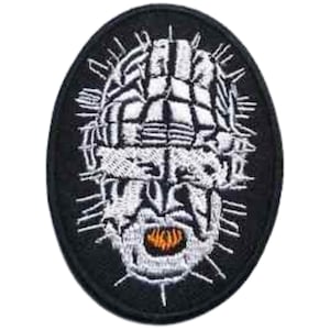 May include: Black and white embroidered patch of a face with a crown of thorns. The face is white with a black background. The patch is oval shaped.