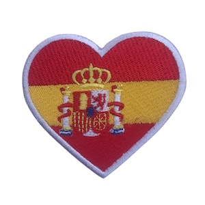 Puede incluir: Parche bordado en forma de corazón con el diseño de la bandera española. El parche tiene una parte superior roja, una sección media amarilla y un borde blanco. El escudo de armas español está en el centro.