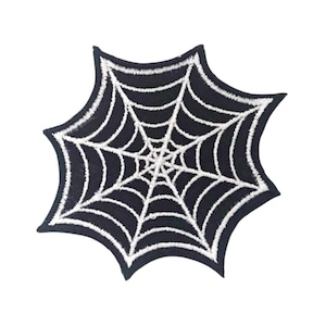 Pode incluir: Patch bordado de teia de aranha preto e branco. A teia é branca e o fundo é preto.
