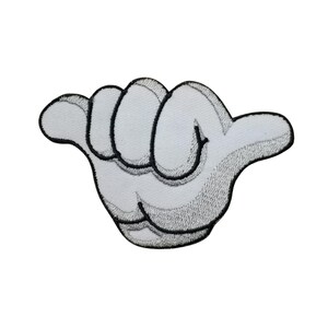 Op de afbeelding: Witte geborduurde patch in de vorm van een hand die het shaka-teken maakt. De patch heeft een zwarte omtrek en een grijs geborduurde textuur. De vingers zijn licht gebogen en de duim is uitgestrekt.