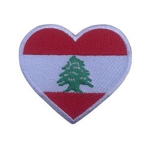 Puede incluir: Un parche bordado en forma de corazón rojo, blanco y verde con la bandera del Líbano. La bandera presenta un cedro verde sobre un fondo blanco con rayas rojas en la parte superior e inferior.