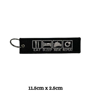 Puede incluir: Llavero negro con un diseño bordado en blanco que dice "Eat Sleep Ride Repeat". El diseño incluye un tenedor y un cuchillo, una cama, una motocicleta y una flecha circular. El llavero mide 11,5 cm por 2,5 cm.