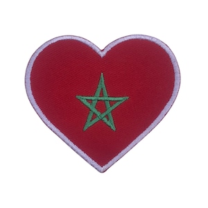 Può includere: Una toppa a forma di cuore con la bandiera marocchina. La toppa ha uno sfondo rosso con un bordo bianco. Una stella verde a cinque punte è centrata sul cuore rosso, che rappresenta l'emblema della bandiera.