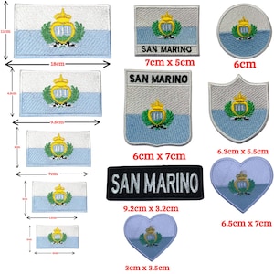 Peut inclure: Une collection d'écussons brodés représentant le drapeau de Saint-Marin dans diverses formes et tailles, incluant des designs rectangulaires, circulaires, en écu et en cœur. Certains écussons affichent le texte SAN MARINO brodé en noir ou blanc.