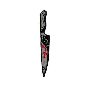 May include: A black and white embroidered patch of a knife with a red blood stain.
