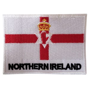 Puede incluir: Parche bordado rectangular con la bandera de Irlanda del Norte. El diseño presenta un fondo blanco, una cruz roja, una mano roja coronada y el texto "NORTHERN IRELAND" en negro.