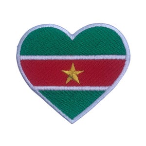 Puede incluir: Un parche en forma de corazón con la bandera de Surinam. La bandera tiene un fondo verde con una franja roja y una estrella amarilla de cinco puntas en el centro.