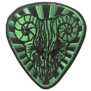 Może przedstawiać: Zielono-czarna, haftowana naszywka w kształcie kostki do gitary. Naszywka przedstawia stylizowany wzór głowy barana ze spiralnymi rogami i promienistym wzorem słonecznym. Wzór jest szczegółowy czarną nicią na zielonym tle.