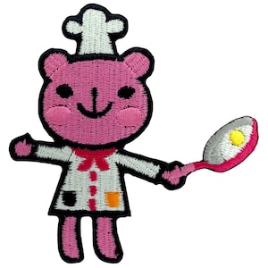 Può includere: Orso di cartone rosa ricamato con un cappello da chef bianco e che tiene una padella rossa e bianca con un uovo giallo all'interno.