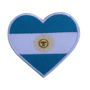 Può includere: Una toppa a forma di cuore con la bandiera argentina. La bandiera è blu e bianca con un sole giallo al centro.