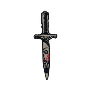 May include: A black and white embroidered patch of a dagger with a red eye and a red streak of blood on the blade.