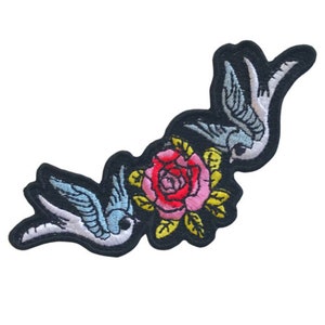 May include: Embroidered iron-on patch featuring two blue and white birds flying around a pink and yellow rose.