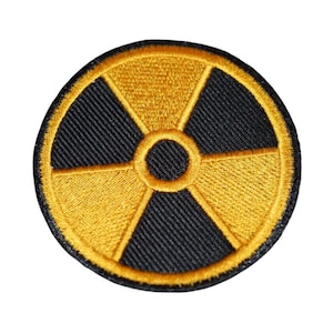 Puede incluir: Un parche bordado amarillo y negro con un símbolo de radiación.