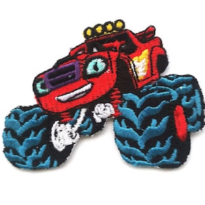 Pode incluir: Caminhão monstro vermelho com pneus azuis e um rosto sorridente. O caminhão tem uma luz amarela no topo e uma chama branca no lado.