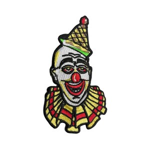 May include: An embroidered iron-on patch featuring a creepy clown with a red nose and a wide smile. The clown is wearing a yellow and red ruffled collar and a cone-shaped hat.