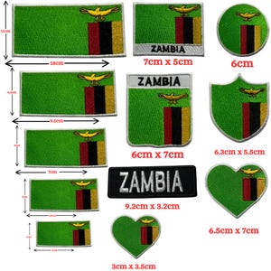 May include: A collection of embroidered patches featuring the flag of Zambia. The patches come in various shapes, including rectangles, circles, and hearts. The flag design includes green, red, black, and gold colors, with the word "ZAMBIA" on some.