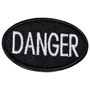 May include: Black oval patch with the word "DANGER" embroidered in white. The patch has a textured surface and a stitched border. The text is in a bold, sans-serif font.
