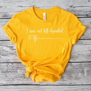 Pu&ograve; includere: Una maglietta gialla con il testo "I am not left-handed" in lettere bianche e un grafico di spada bianca.