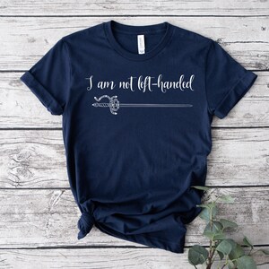 Pu&ograve; includere: Una maglietta blu navy con una grafica bianca di una spada e il testo "Non sono mancino".