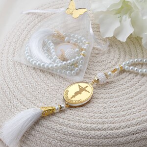 May include: White pearl rosary with a gold charm that says "God Bless You" and a white tassel. The rosary is in a white organza bag with a gold butterfly.