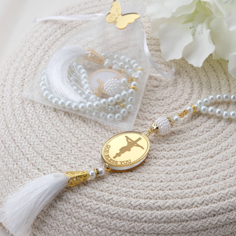 May include: White pearl rosary with a gold charm that says "God Bless You" and a white tassel. The rosary is in a white organza bag with a gold butterfly.