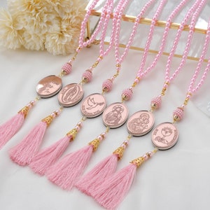 May include: Set of five pink pearl rosaries with gold accents and different religious medallions. Each rosary has a pink tassel.
