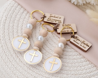 Puede incluir: Tres llaveros de madera con dijes de cruz dorada y cuentas blancas. Cada llavero tiene una etiqueta de madera personalizada con el texto "Isabel's First Communion February 26, 2023", "Mi Bautizo Enero 26, 2023" y "Sofia's Baptism February 26, 2023".