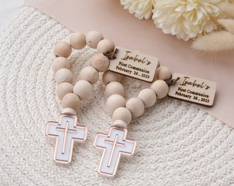 May include: Wooden beaded rosary with two wooden tags that read "Isabel's First Communion February 26, 2023". The rosary has two white crosses with a rose gold outline.