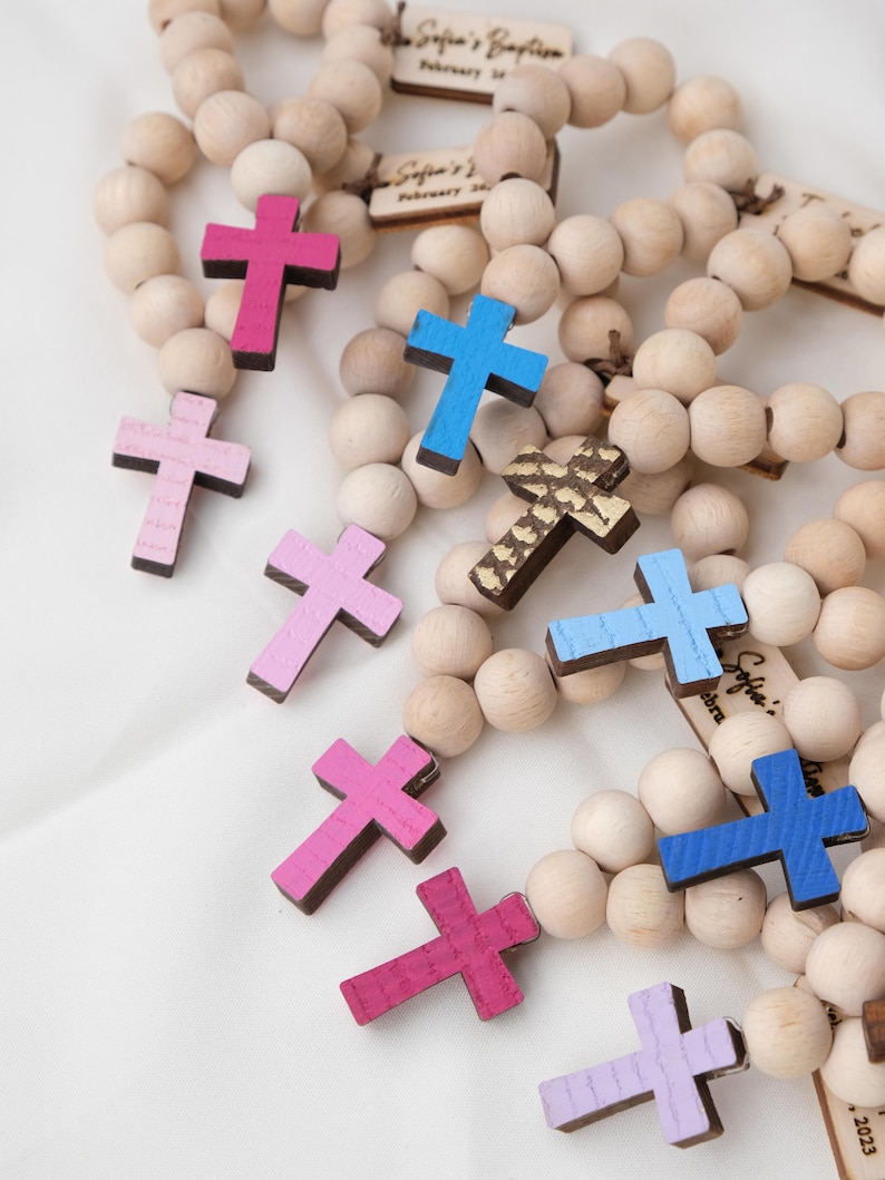 May include: Wooden bead rosaries with colorful painted crosses in shades of pink, blue, and gold. Each rosary features a wooden tag with the text "Sofia's Baptism" and the date "February 2023".