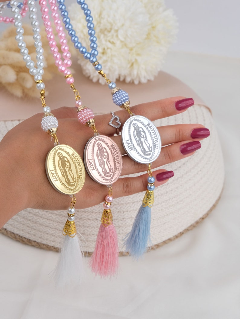 Puede incluir: Tres collares de cuentas con medallones dorados que representan la imagen de la Virgen Mar&iacute;a. Cada collar tiene un borla de un color diferente: blanco, rosa y azul.