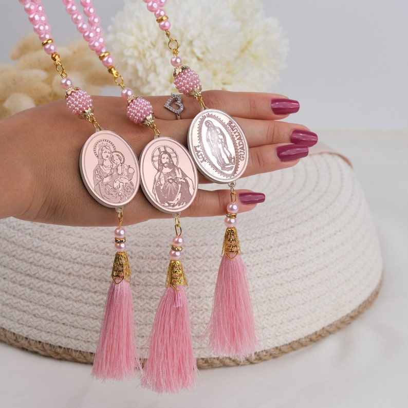 Puede incluir: Tres medallones religiosos de color rosa y dorado con borlas. Los medallones muestran im&aacute;genes de Jes&uacute;s, Mar&iacute;a y la Virgen Mar&iacute;a.