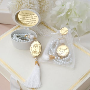 May include: Two white pearl rosaries with gold charms. One charm features a dove with an olive branch and the text "God Bless You". The other charm features a chalice and the text "Holy Communion".