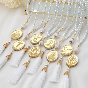 Puede incluir: Ocho collares de perlas blancas con detalles dorados y dijes ovalados con im&aacute;genes religiosas. Los dijes tienen letras doradas que dicen "Jes&uacute;s & Yo", "Que Dios te bendiga", "Primera Comuni&oacute;n", "Primera Comuni&oacute;n", "Que Dios te bendiga", "Santa Mar&iacute;a" y "Ocasi&oacute;n especial".