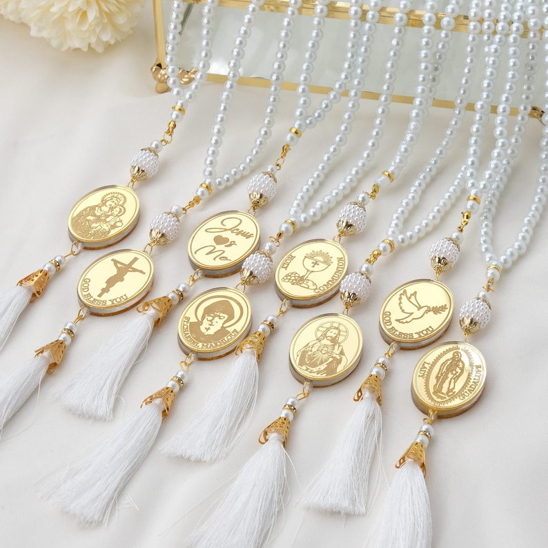 Puede incluir: Ocho collares de perlas blancas con detalles dorados y dijes ovalados con im&aacute;genes religiosas. Los dijes tienen letras doradas que dicen "Jes&uacute;s & Yo", "Que Dios te bendiga", "Primera Comuni&oacute;n", "Primera Comuni&oacute;n", "Que Dios te bendiga", "Santa Mar&iacute;a" y "Ocasi&oacute;n especial".