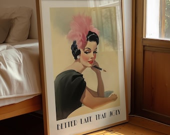 May include: A framed art print featuring a stylized illustration of a person with dark hair wearing a pink feather headpiece and a black top. The person holds a pen to their chin. The text "BETTER LATE THAN UGLY" is printed in black at the bottom.