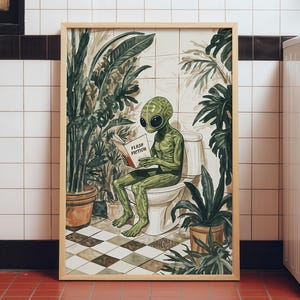 May include: A framed art print featuring a green alien sitting on a white toilet in a tiled bathroom, reading a book titled Flush Fiction. The scene includes large potted green plants on a chequered floor, rendered in a detailed illustrative style.